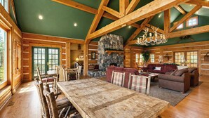A log cabin interior with a stone fireplace, wooden furniture, and a high ceiling.