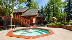 A wooden cabin with a hot tub, wooden deck, and a staircase leading to the entrance.