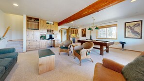A spacious living area with a pool table, wicker chairs, a sofa, and a kitchen with wooden cabinets. - Luxury McCall Home | Views, Game Room, Deck, Pool (McCall)