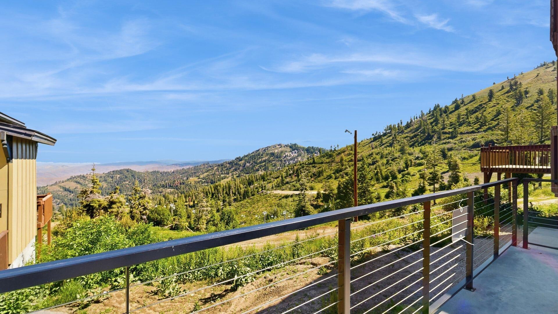 Un balcon offrant une vue sur un paysage montagneux, une terrasse en bois et une rambarde en métal.