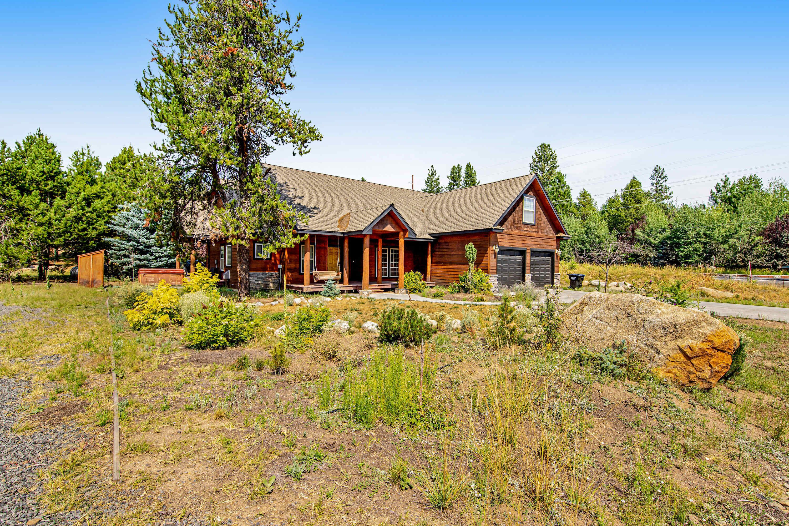 A log cabin with a front porch, a garage, and a large rock in the yard.