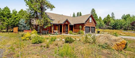 A log cabin with a front porch, a garage, and a large rock in the yard.