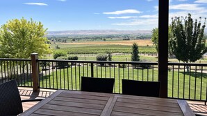 Eine Holzterrasse mit Tisch und Stühlen mit Blick auf einen Weinberg und die ferne Hügellandschaft.