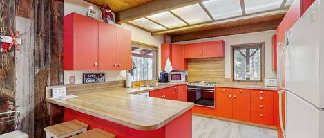 A compact kitchen with red cabinets, a wooden countertop, and a built-in stove.