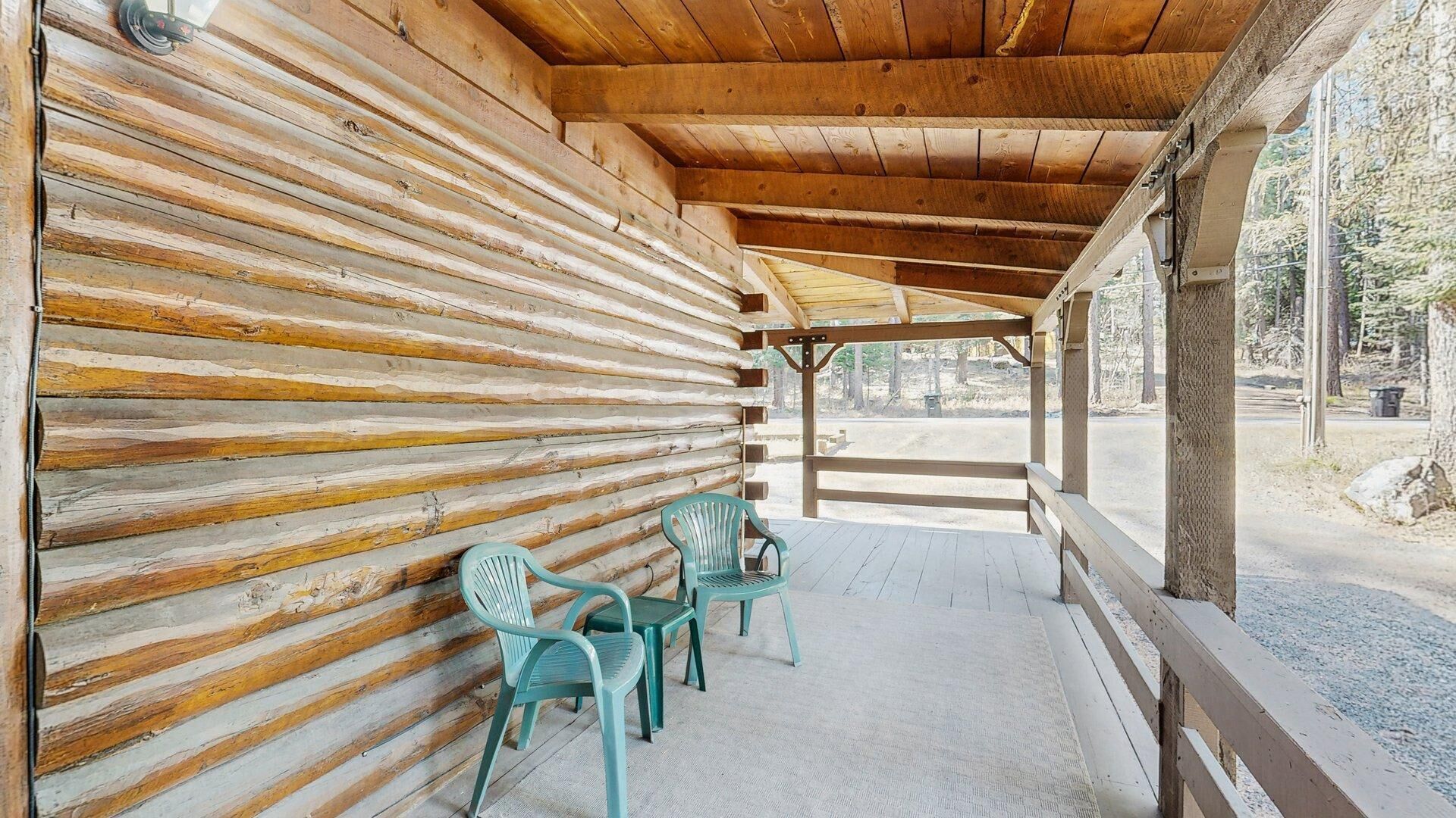 Eine Blockhütte mit überdachter Veranda, Holzwänden und zwei grünen Stühlen.