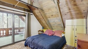 Un dormitorio con una cama grande, techo de madera, puerta corrediza de vidrio y cómoda amarilla.