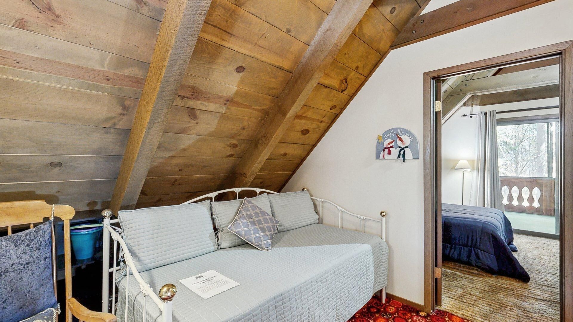Een slaapkamer met een schuine kap, een bed met een gewatteerde spreidekbed, een nachtkastje met een lamp en een raam met uitzicht op de omgeving.