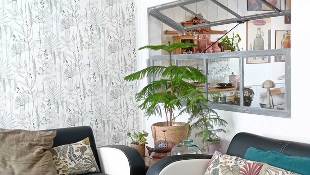Un salon avec un canapé en cuir noir, une table basse ronde en bois et une lampe suspendue en osier.