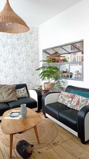 Un salon avec un canapé en cuir noir, une table basse ronde en bois et une lampe suspendue en osier.