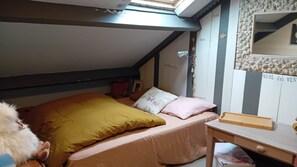 Un dormitorio con techo inclinado, una cama con muchas almohadas, una mesita y una pared decorada.