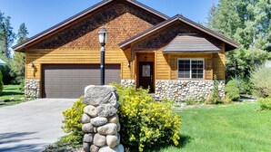 A wooden house with a stone foundation, a garage, and a well-maintained lawn. - McCall Golf Home | Patio, Fenced Yard & Views (McCall)