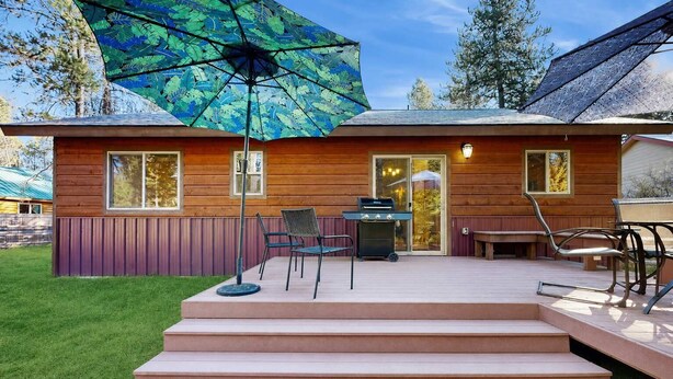 Una cabaña de madera con un porche, mobiliario exterior y una parrilla.