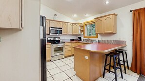 Una cocina moderna con armarios de madera, un refrigerador de acero inoxidable, un microondas, un horno y una isla grande con taburetes.