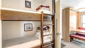 Un lit superposé avec une échelle, un petit bureau et une porte donnant sur une salle de bain.