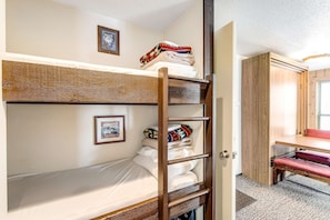 A bunk bed with a ladder, a small desk, and a door leading to a bathroom.