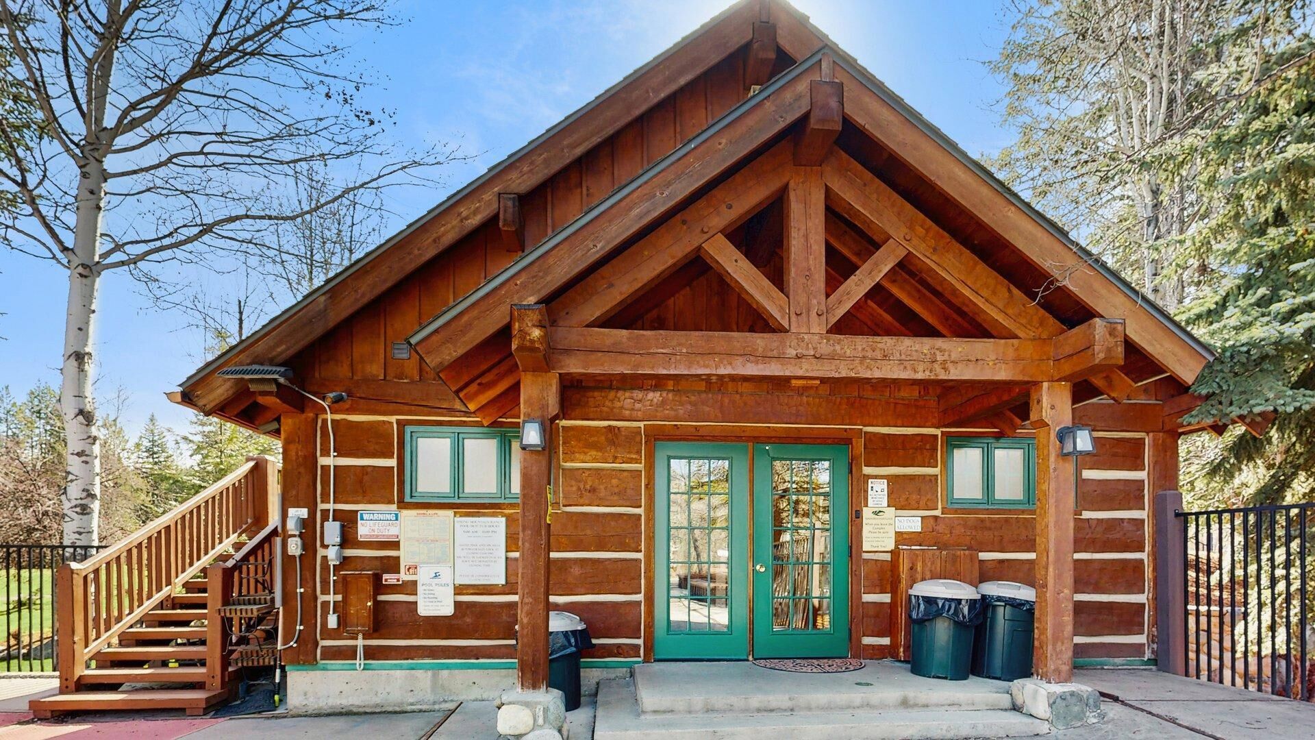 Une cabane en bois avec une porte verte, un escalier et des poubelles à l’extérieur.