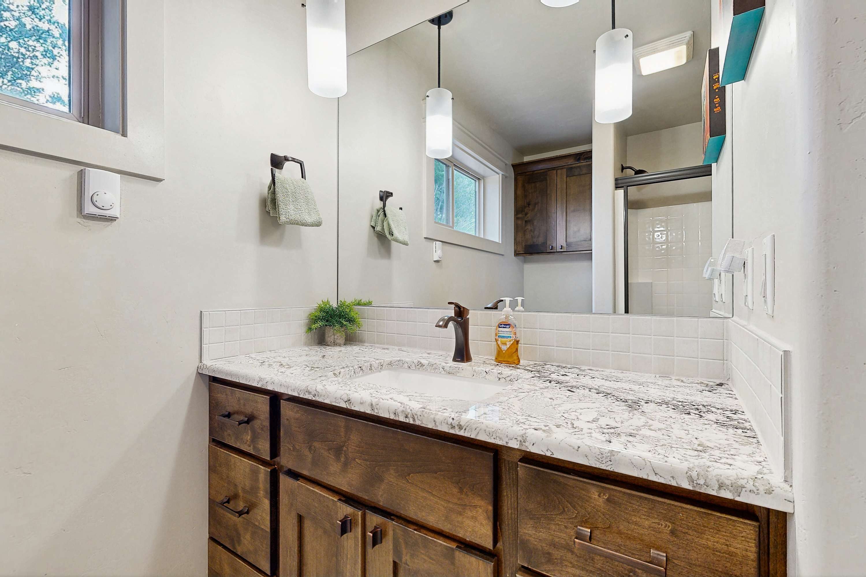 A bathroom with a marble sink, wooden cabinets, a large mirror, and pendant lights.