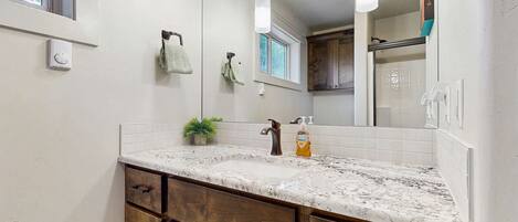 A bathroom with a marble sink, wooden cabinets, a large mirror, and pendant lights.
