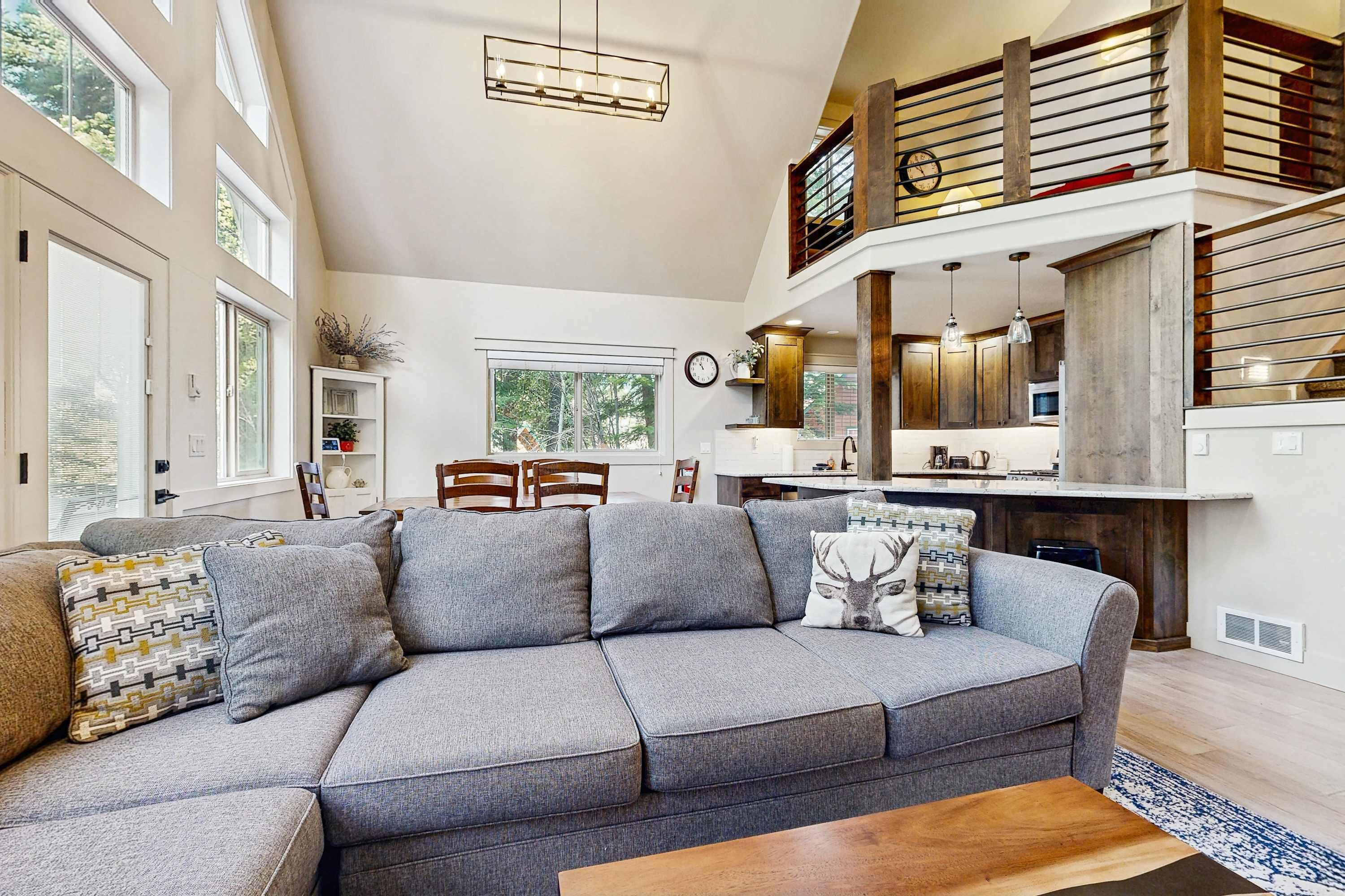 A spacious living area with a large gray sectional sofa, a wooden coffee table, and a dining area with wooden chairs.
