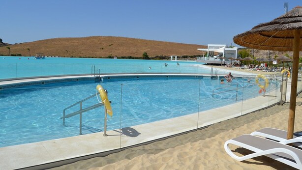 A swimming pool with clear blue water, surrounded by a sandy beach area with lounge chairs and umbrellas. - Estepona Garden Apartment for 3 (Casares)