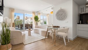 A modern living room with a glass dining table, white sofas, and a large decorative wall piece. - Estepona Garden Apartment for 3 (Casares)