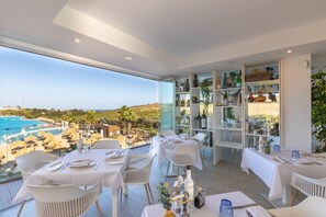 A dining area with tables set for two, overlooking a pool and a scenic landscape. - Estepona Garden Apartment for 3 (Casares)
