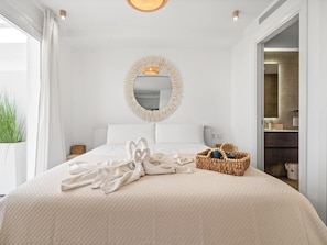 A hotel room with a large bed, a round mirror, a basket of toiletries, and a view of the bathroom. - Estepona Garden Apartment for 3 (Casares)