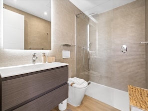 A modern bathroom with a glass-enclosed shower, a large mirror, and a vanity with a dark wood cabinet. - Estepona Garden Apartment for 3 (Casares)