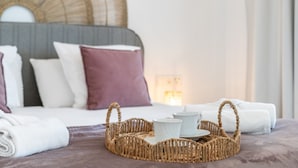 Ein ordentlich bezogenes Bett mit einem Korb, der Teekanne, Tassen, Kissen und eine Decke enthält, und einem Kopfteil.