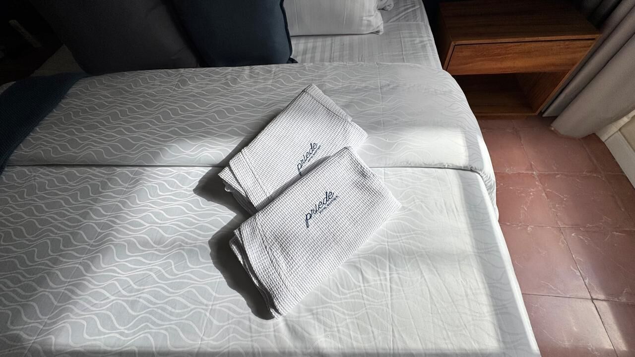 Una cama bien tendida con ropa de cama estampada y dos toallas dobladas con la palabra 'poderosa' en ellas.