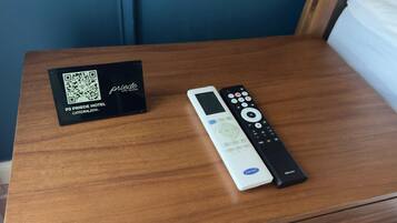 Une chambre d’hôtel avec une table en bois, un code QR pour l’hôtel P3 Priebe et une télécommande.