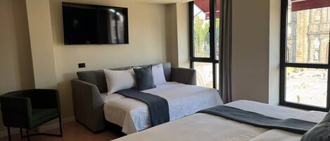 A hotel room with a bed, a sofa, a TV, and a window with a view of a building.
