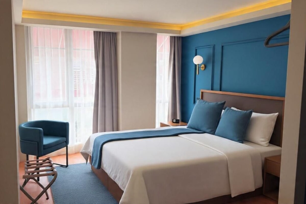 Una habitación de hotel con una cama, una silla, una mesita de noche y una ventana con cortinas.