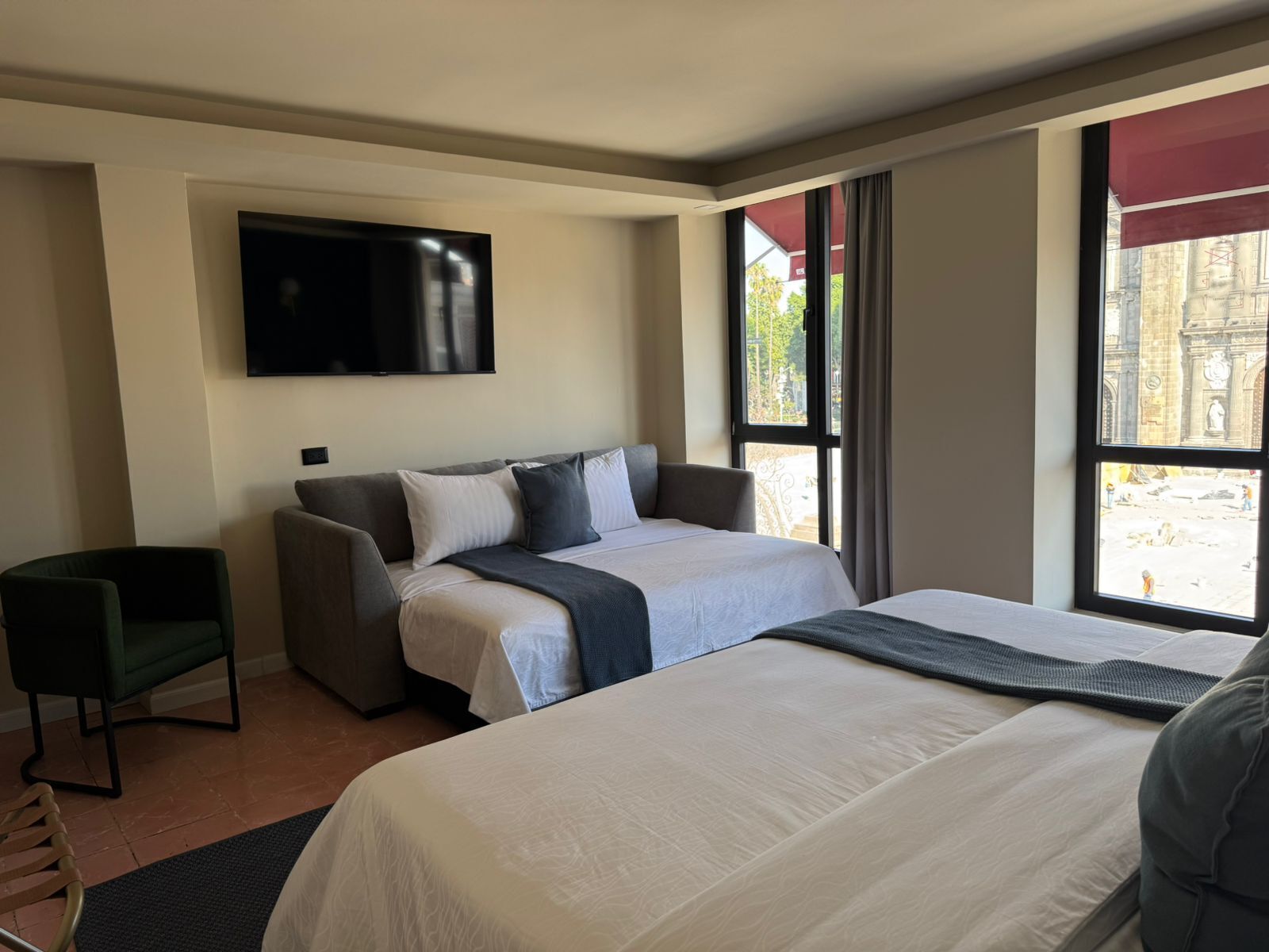 A hotel room with a bed, a sofa, a TV, and a window with a view of a building.