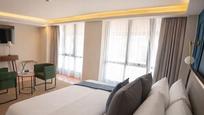 A hotel room with a large bed, a desk with a chair, a TV, and a view of the outdoors. - PRIEDE HOTEL BOUTIQUE (Puebla)