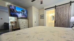 A bedroom with a large bed, a dresser, a television, a sliding door, and a bathroom visible through the door. - Sand Dollar 6mi-Pensacola Bch (Gulf Breeze)