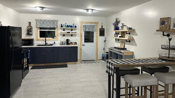 A modern kitchen with dark cabinets, a black refrigerator, and a wooden dining table with bar stools. - Whitsendsport  unit 4  1 bedroom & queen pull out  couch on  50 acres Smithfield (Smithfield)