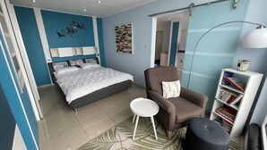 Un dormitorio con cama, una silla, una mesita de noche, una estantería y un espejo.