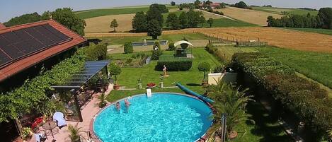 A swimming pool with a surrounding deck, a covered patio area, and a view of the countryside.
