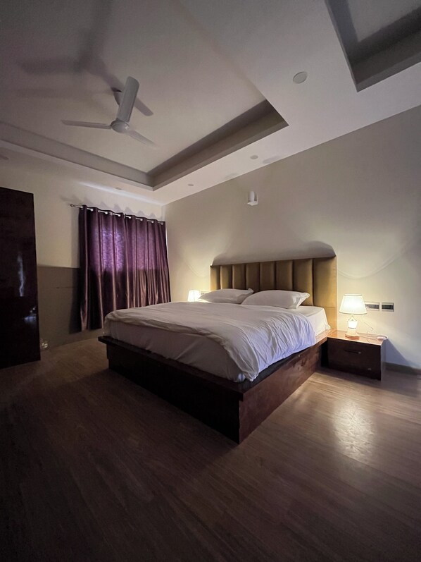 Un dormitorio moderno con una cama grande, un ventilador de techo y una mesita de noche con lámpara.