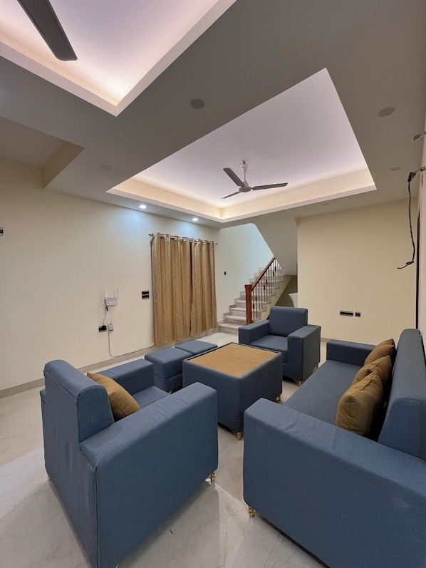 A modern living room with blue sofas, a ceiling fan, and a staircase leading to an upper level.