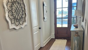 Um corredor com piso de madeira, porta branca, um detalhe decorativo na parede e vista através de uma porta de vidro.