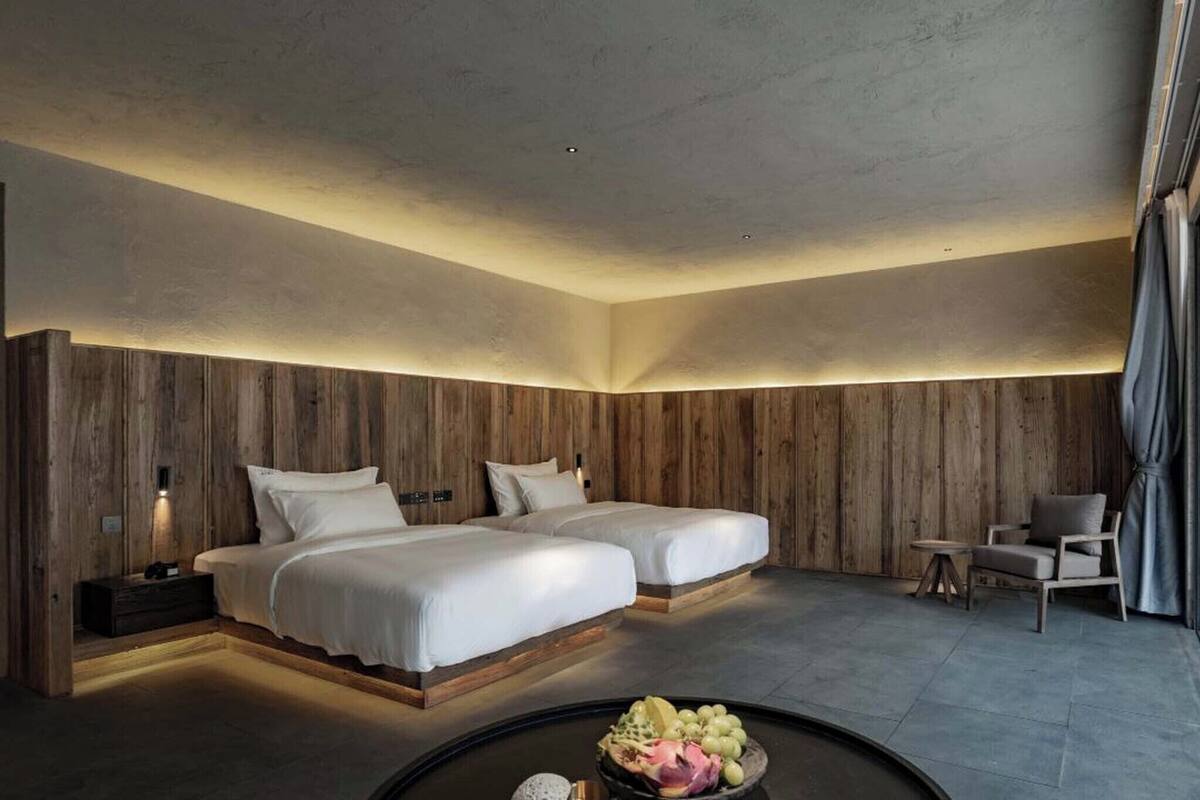 A modern hotel room with two beds, a small seating area, and a dining table with fruit.