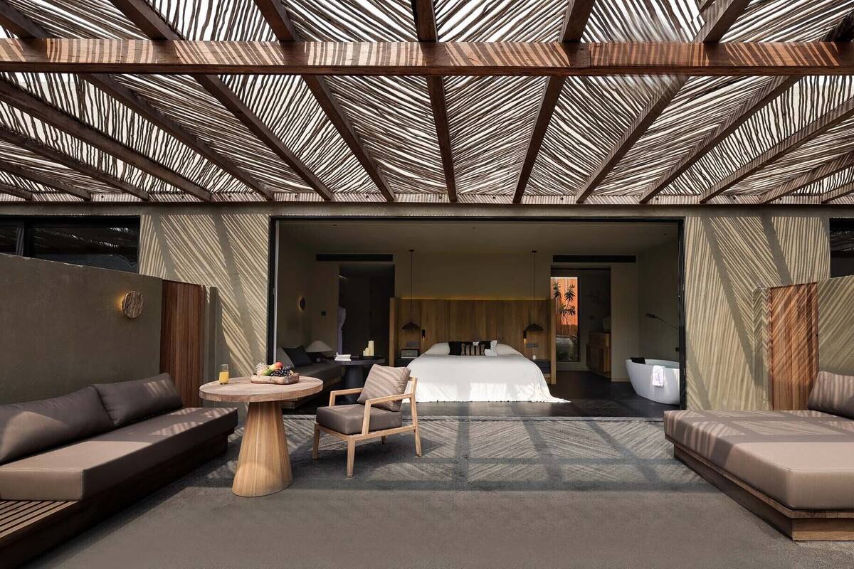 A modern hotel room with a large bed, two sofas, a round table, and a ceiling with a geometric pattern.