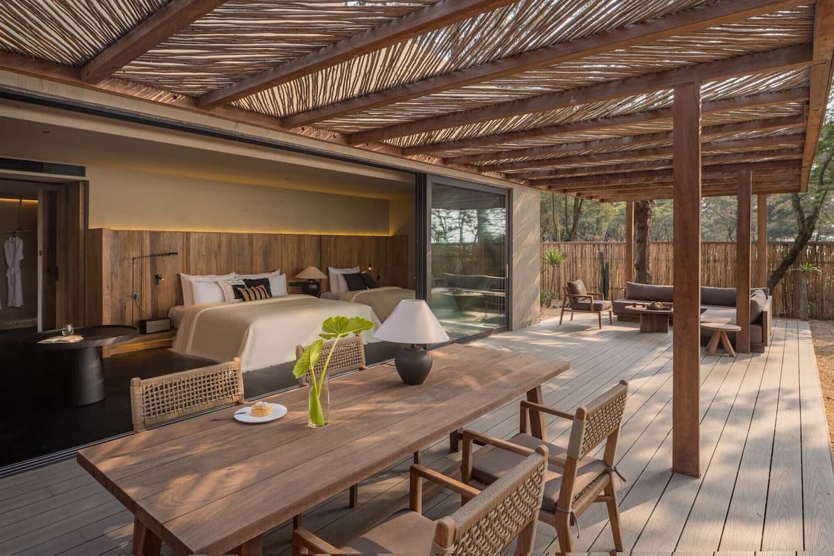 A modern outdoor bedroom with a wooden deck, a dining table, and a sofa area.