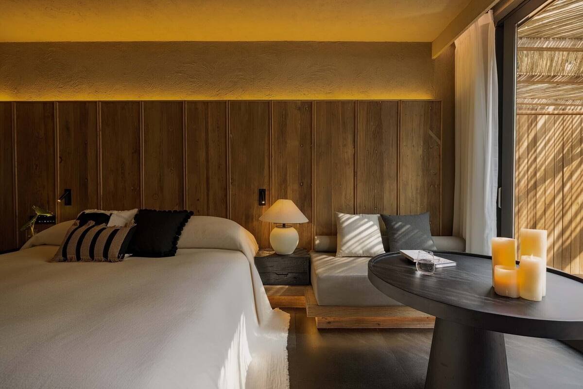 A hotel room with a bed, a sofa, a nightstand with a lamp, and a round table with candles.
