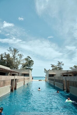 A swimming pool with wooden deck areas, a clear view of the sea, and a bridge in the distance. - Weizhou Island Coral Reef Hotel (Beihai)
