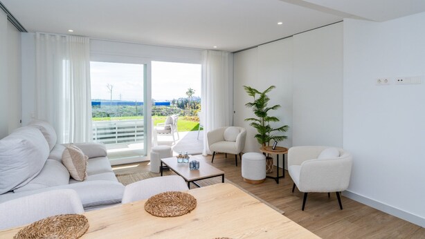 A modern living room with a sofa, armchairs, a coffee table, and a view of a balcony with outdoor furniture. - Garden Apartment at Alcazaba Lagoon (Casares)
