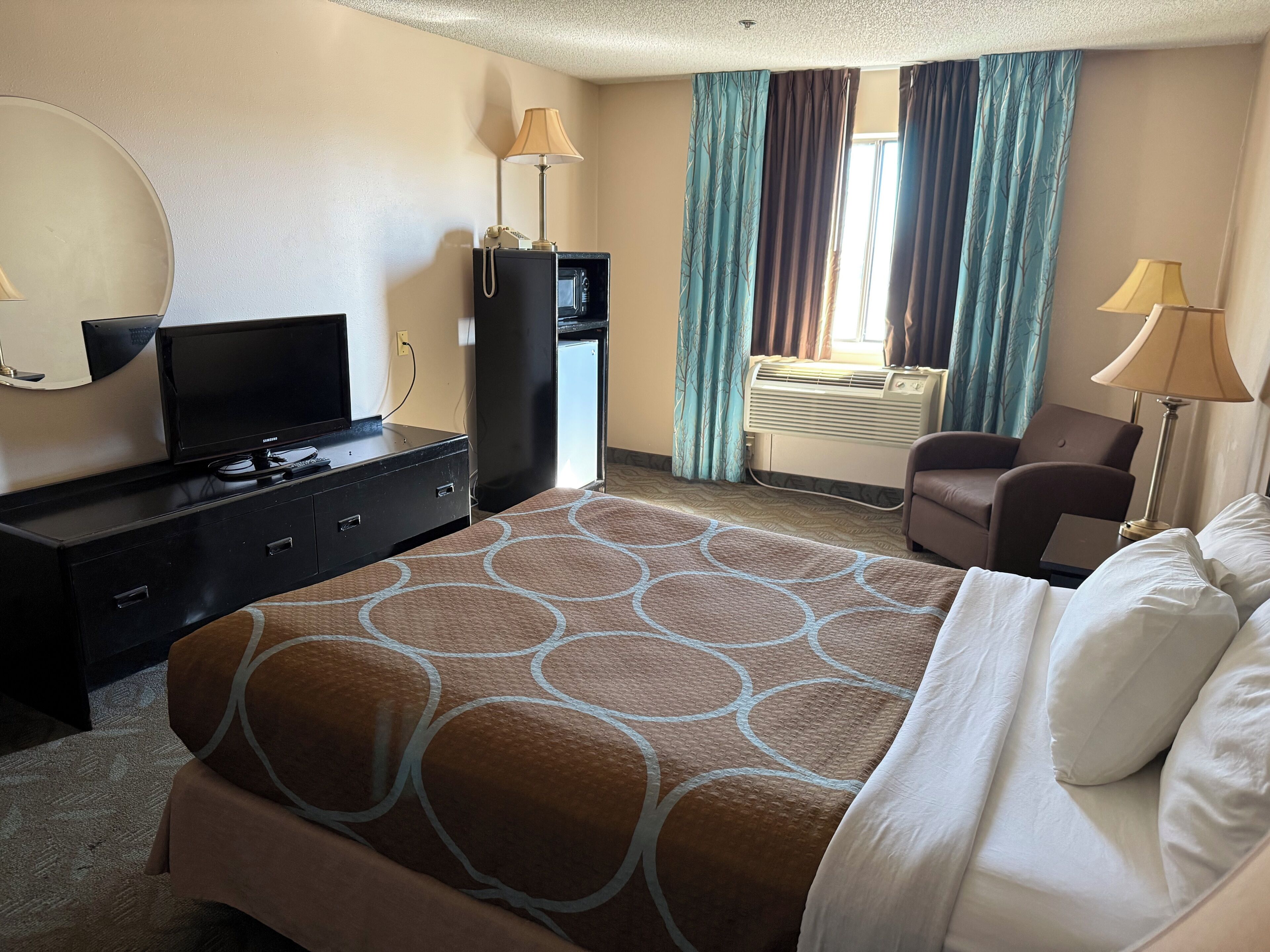 Une chambre d’hôtel avec un lit, une télévision, un bureau, une chaise et une fenêtre avec des rideaux.