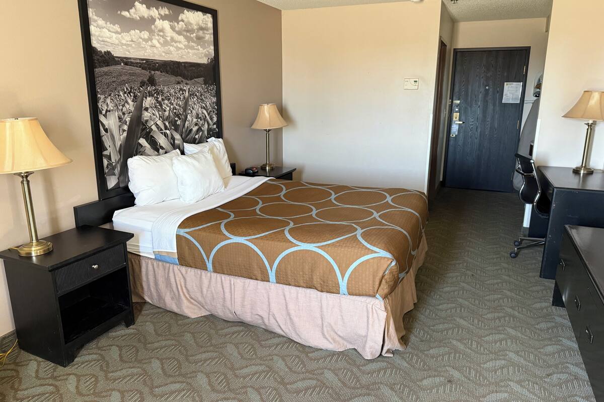 Una camera d'albergo con un letto, due lampade ai comodini, una scrivania e una sedia.